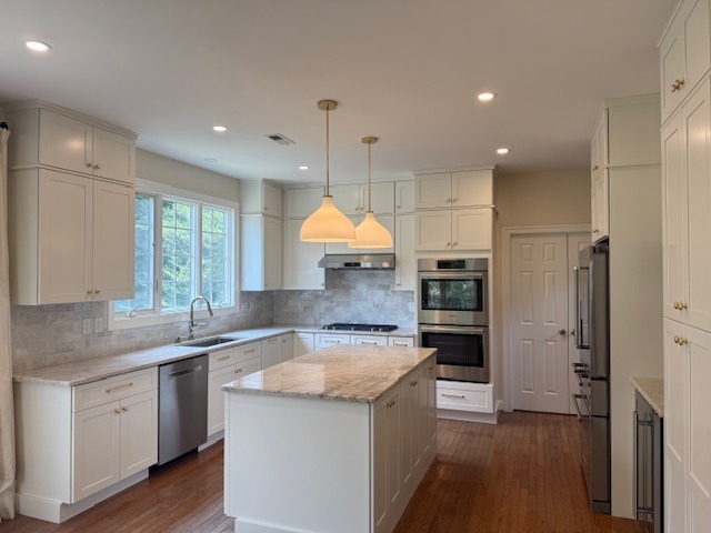 a bright kitchen remodel done by Rose Tree Construction that has white cabinets, light gray stone backlash and a marble topped kitchen island.